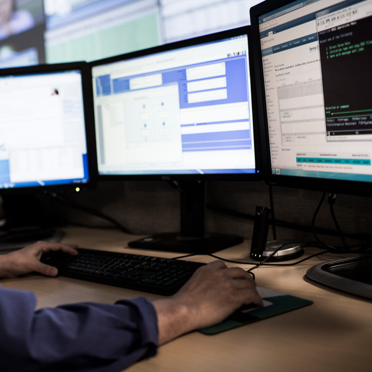 Computer operator in front of three screens